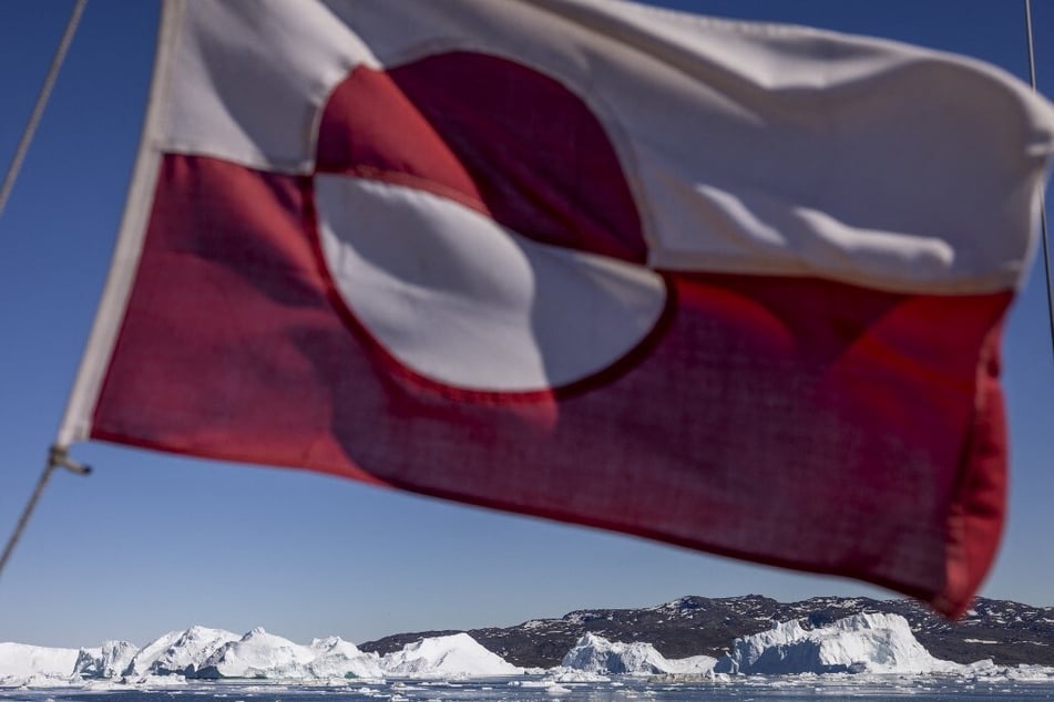 A Greenlandic flag flutters on a boat sailing among icebergs in Disko Bay, Ilulissat, western Greenland.