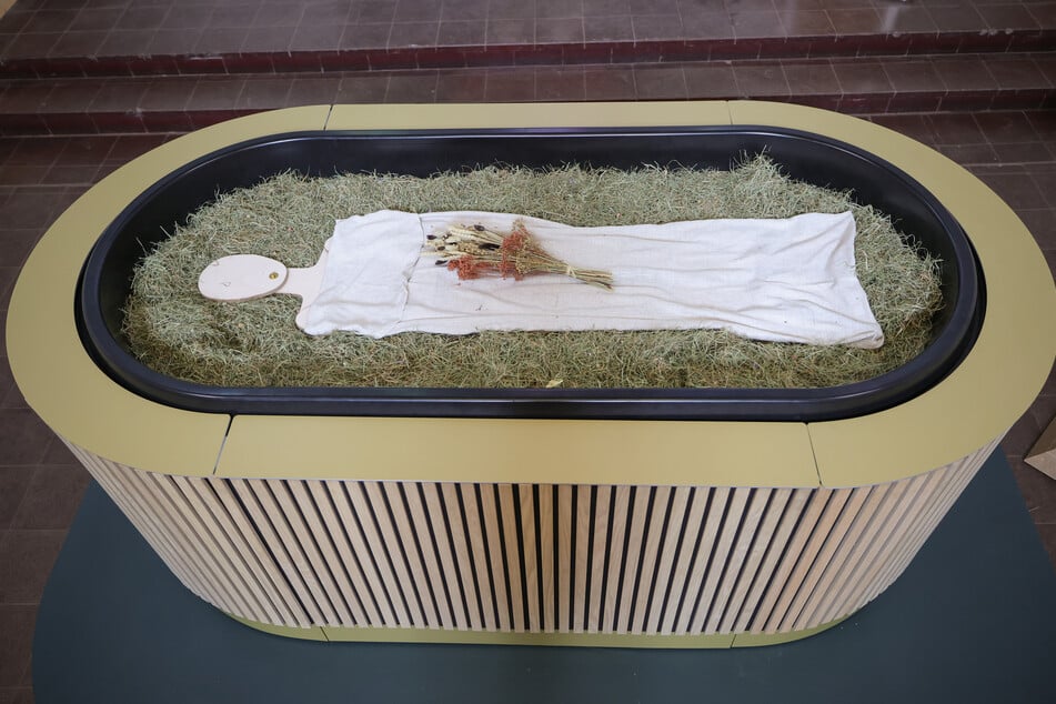 Heu, Stroh, Blumen und eine Holzfigur liegen in einem sogenannten "Kokon" der neuen Bestattungsform "Reerdigung".