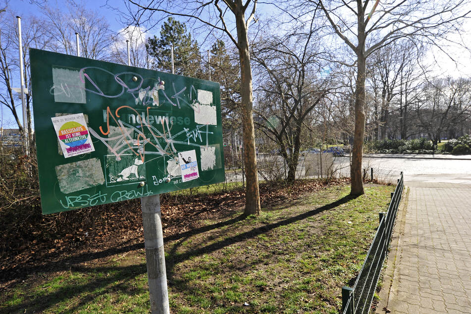 Das Schild der Hundewiese am Schillerplatz ist beschmiert, überklebt und kaum lesbar. Auf der Wiese liegen krustige Tretminen.