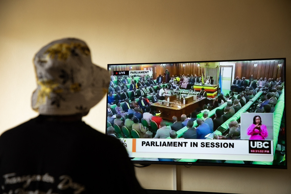 Eine ugandische Transfrau, die kürzlich angegriffen wurde, sieht sich einen Fernsehbildschirm an, auf dem die Live-Übertragung der Sitzung des Parlaments für das Anti-Homosexuellen-Gesetz gezeigt wird.