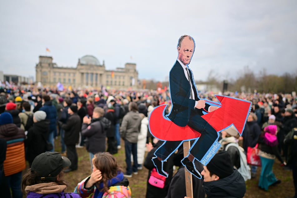 Ein Mann hält während einer Demonstration in Berlin eine Bildmontage von CDU-Kanzlerkandidat Merz (69), der auf einem Logo der AfD reitet.