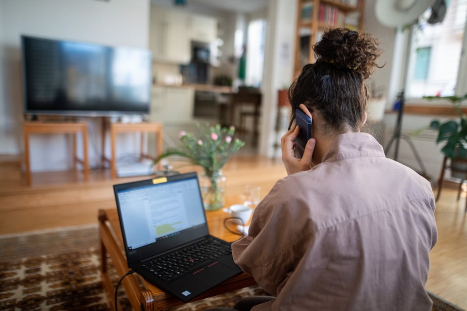 Eine Frau arbeitet im Homeoffice - in ihrem Wohnzimmer - und nimmt an einer Telefonkonferenz teil.