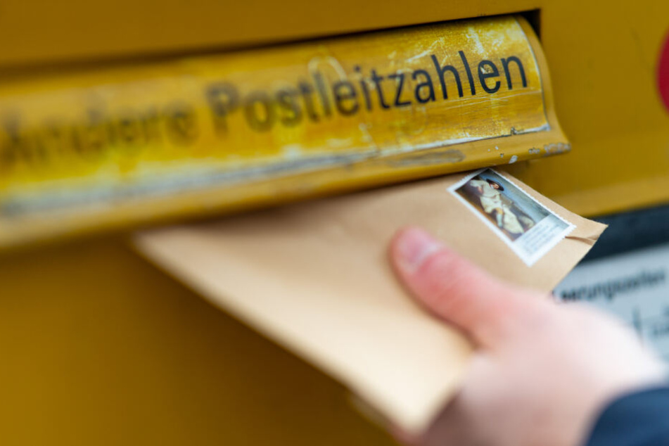 Eine Person wirft einen Briefumschlag in einen Briefkasten. (Symbolbild)