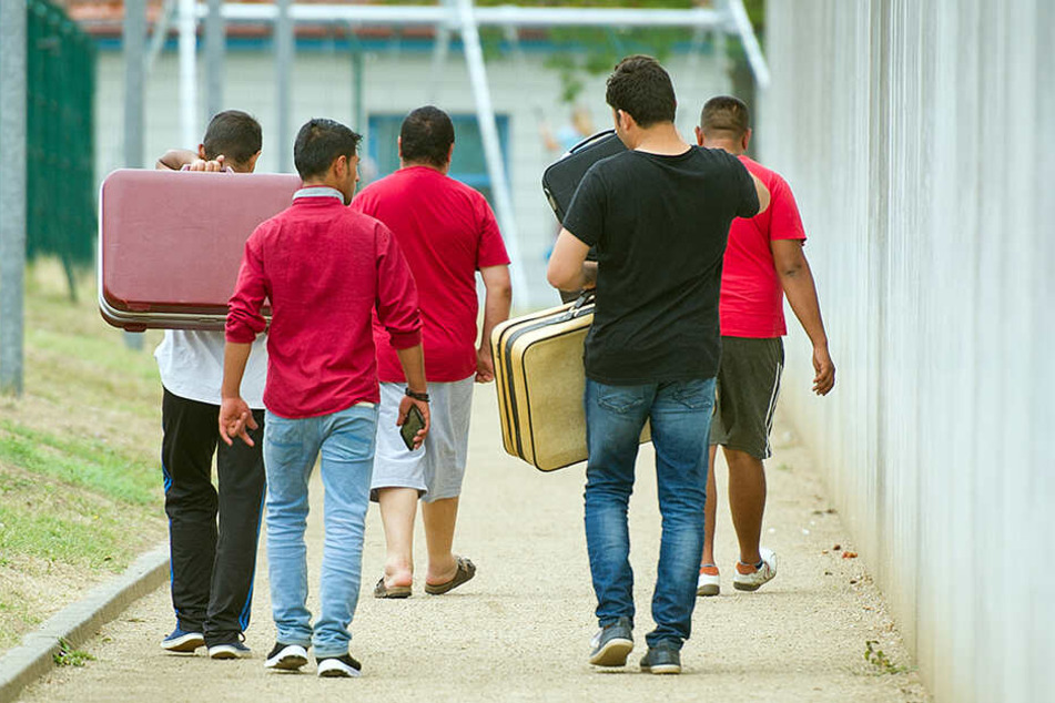 Geflüchtete laufen mit Koffern bepackt auf einem Weg einer Erstaufnahmeeinrichtung für Flüchtlinge in Ingelheim/Rhein.