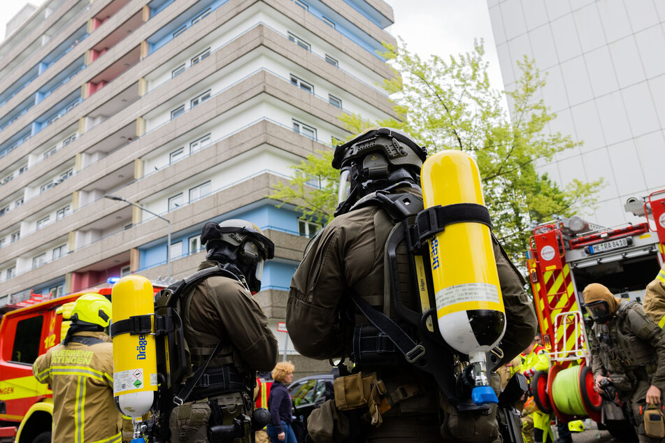 Polizeibeamte mit Gasmasken und Feuerwehrleute stehen vor einem Hochhaus in Ratingen. Insgesamt wurden neun Einsatzkräfte bei der Explosion verletzt.