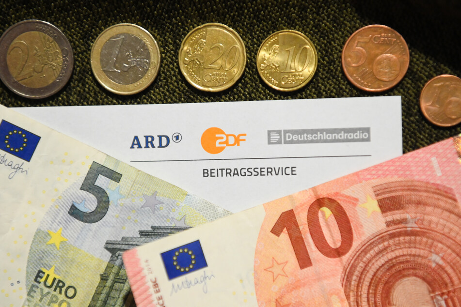 Auf einem Tisch liegt ein Anschreiben und Überweisungsträger für die Rundfunkgebühren, sowie der Betrag von 18 Euro und 36 Cent.
