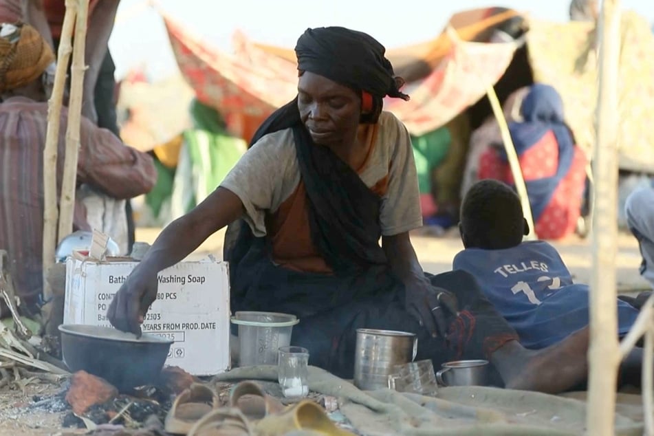 A displaced Sudanese woman makes tea while others gather in makeshift tents in Tawila after fleeing El-Fasher city in Darfur, on October 29, 2025,