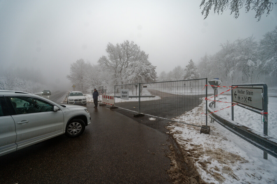 Hellenthal: Besucher im Skigebiet "Weißer Stein" in der Eifel stehen vor einem Bauzaun, der die Zufahrt eines Parkplatzes sperrt.