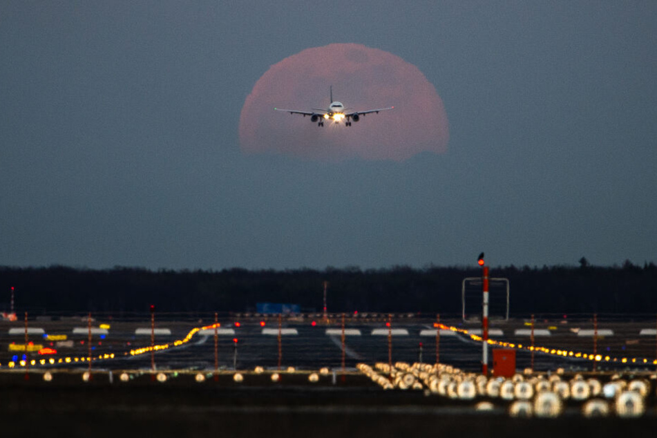 Frankfurt am Main: Ein Passagierflugzeug befindet sich am Frankfurter Flughafen im Landeanflug, während im Hintergrund der Vollmond aufgeht.