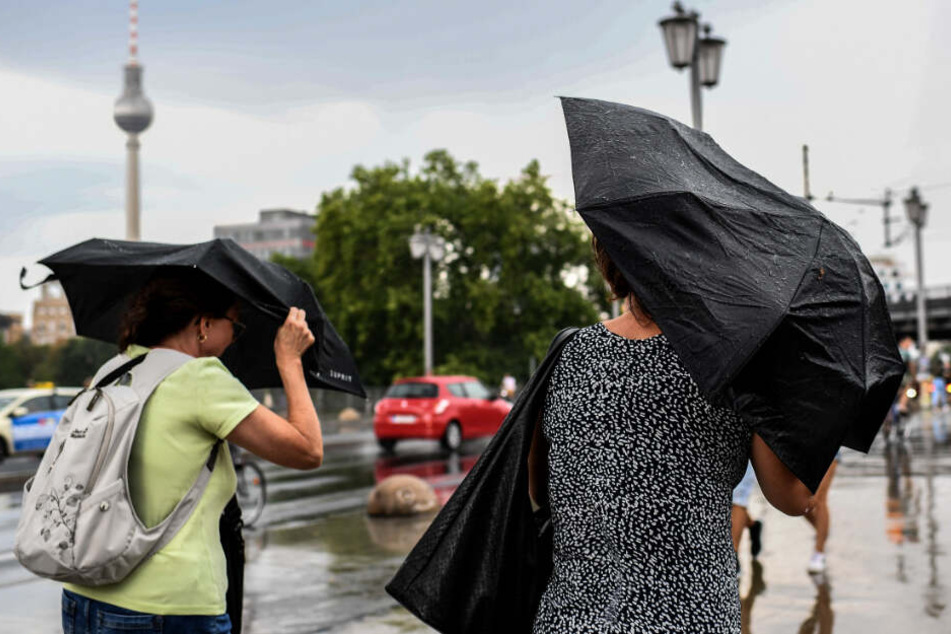 Zwei Frauen versuchen sich vor dem Regen mit Schirmen zu schützen.