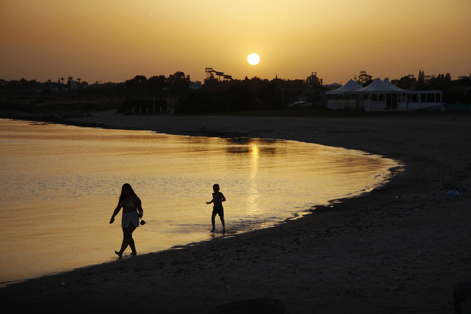 Strandbesucher gehen bei Sonnenuntergang an einem leeren Strandabschnitt des Strandhotels Dome in Zyperns Badeort Ayia Napa spazieren.
