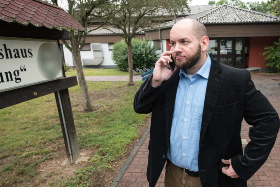 Stefan Jagsch steht vor dem Gemeinschaftshaus im Ortsteil, in dem er gewählt wurde und telefoniert.