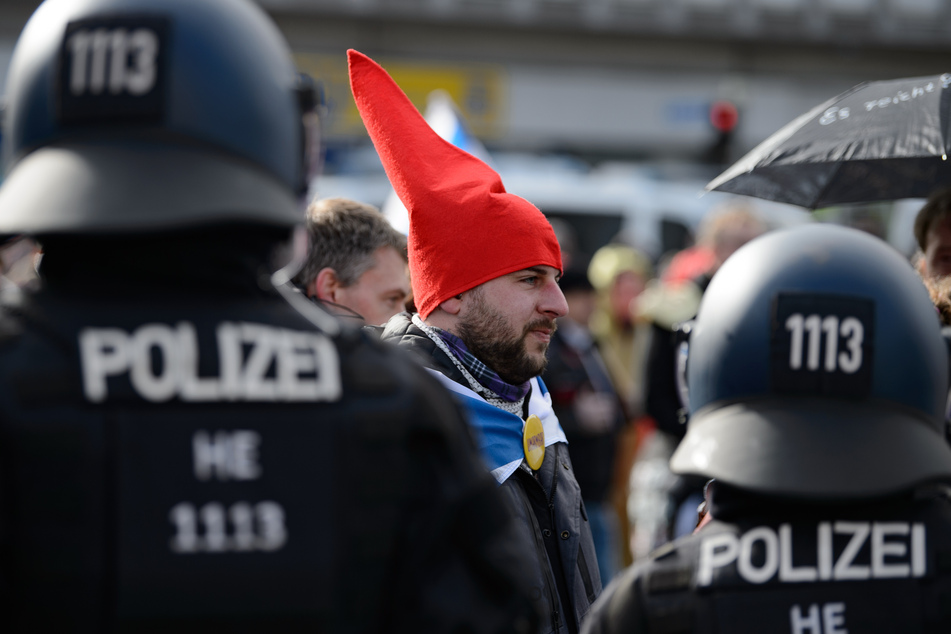 Ein Teilnehmer mit einer roten Zipfelmütze und ohne Mund-Nasen-Bedeckung steht bei einer Kundgebung unter dem Motto "Freie Bürger Kassel - Grundrechte und Demokratie" vor Polizisten.