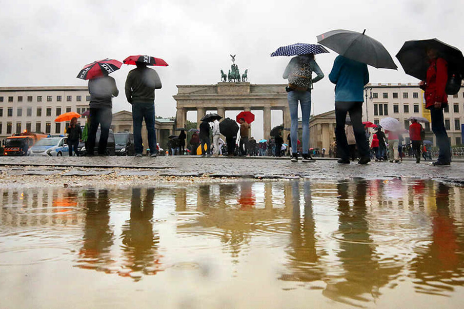 Bei ströhmendem Regen gehen Touristen bei Temperaturen um 16 Grad Celsius am Brandenburger Tor in Berlin vorbei.