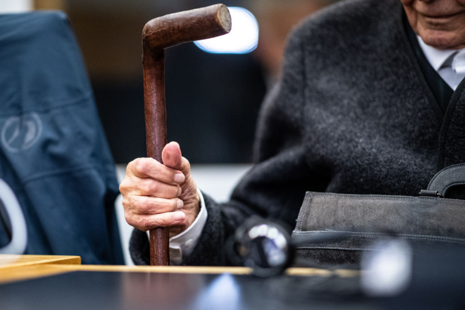 Auf der Anklagebank muss sich der 94-Jährige an einem Stock festhalten.