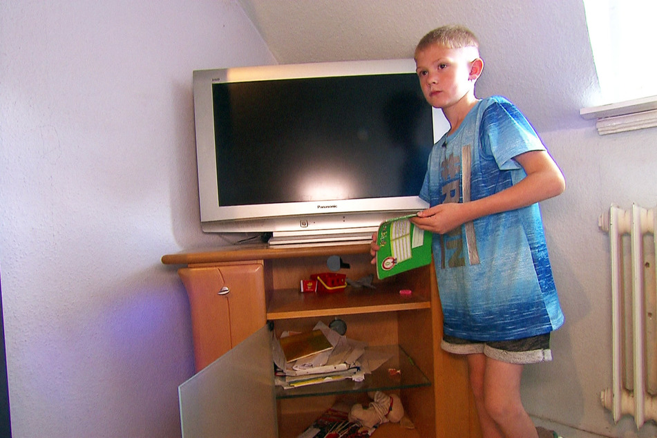 Der älteste Sohn Mirco (7) vor einem TV-Schrank, in dem seine Schulsache ohne jegliche Ordnung umherfliegen.