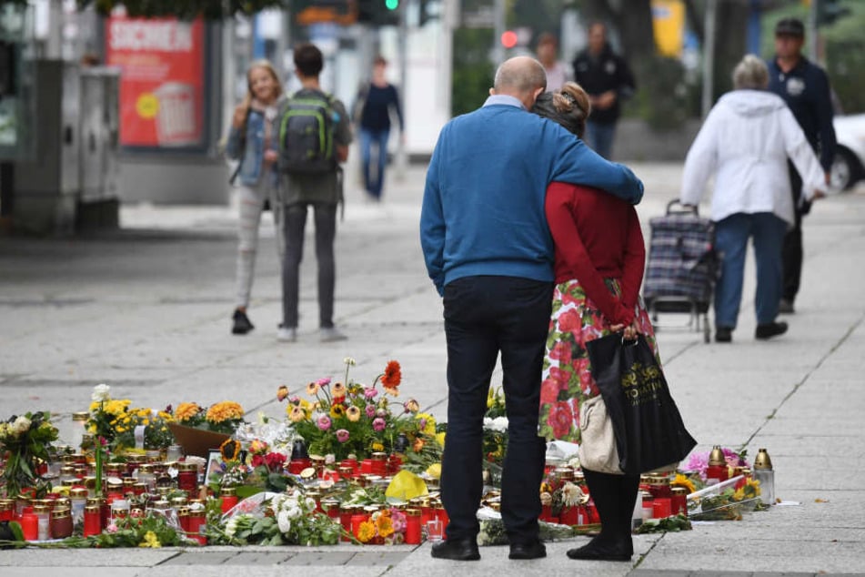 Passanten stehen am Tatort, an dem zahlreiche Blumen und Kerzen niedergelegt wurden.