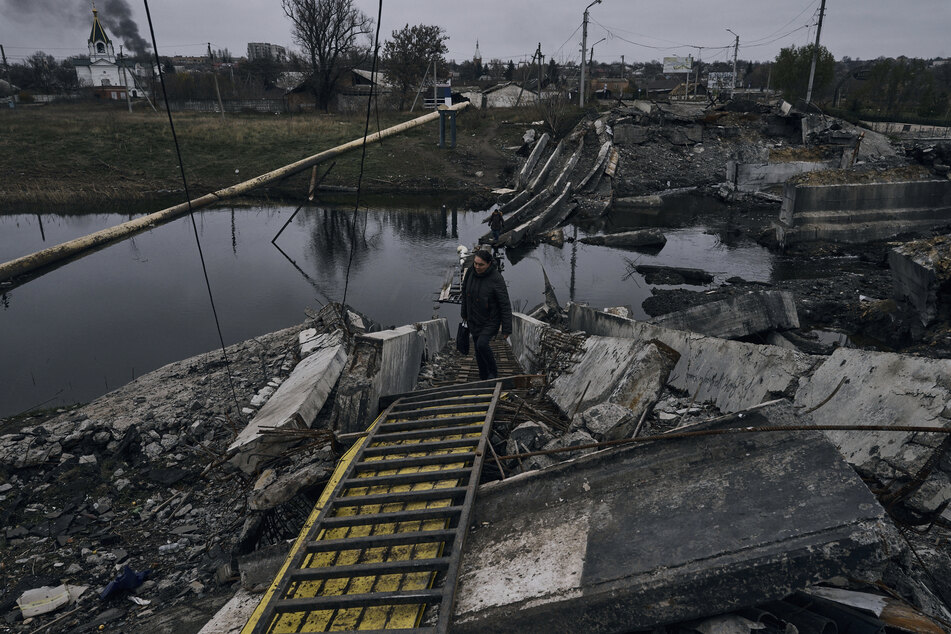 Eine Frau geht über eine explodierte Brücke in Bakhmut in der Region Donezk. Russlands Armee hat Donezk in größeren Teilen erobert und im September - ebenso wie das Nachbargebiet Luhansk sowie Saporischschja und Cherson im Süden - völkerrechtswidrig annektiert.