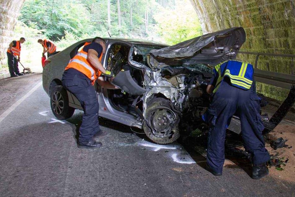 Einsatzkräfte an der Unfallstelle betrachten das völlig zerstörte Auto.