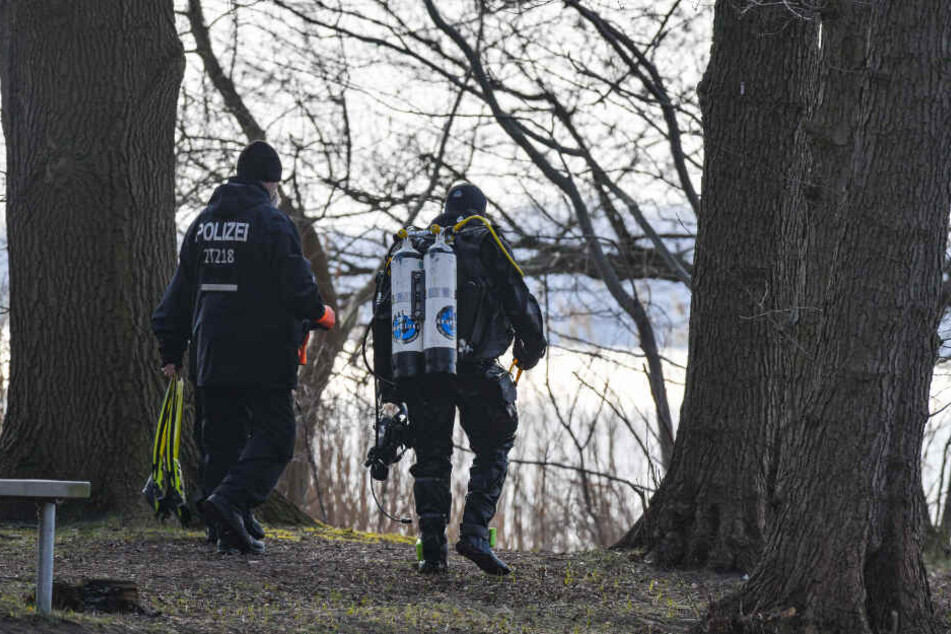 Ein Polizeitaucher geht am Ufer des Wolziger Sees im Landkreis Dahme-Spreewald entlang.