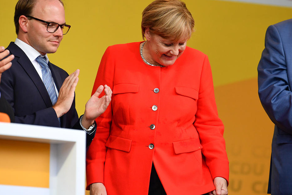 Angela Merkel schaut auf ihren Tomatenfleck und muss lachen.