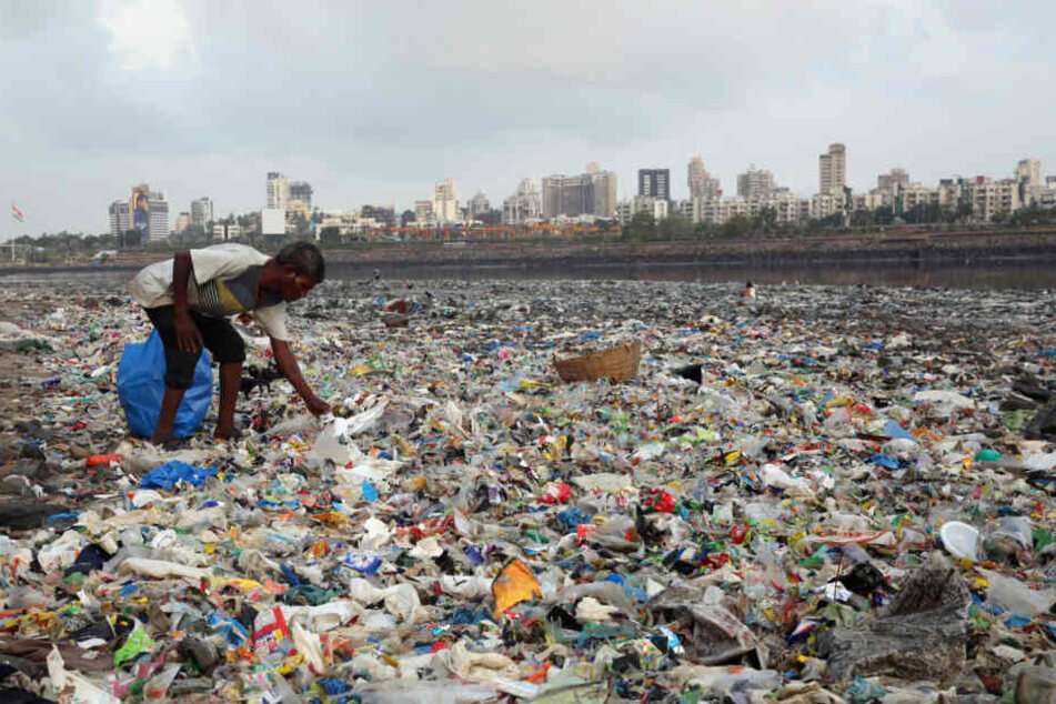 Ein Mann sammelt Plastik und andere wiederverwertbare Materialen an der von Plastiktüten und sonstigen Müll übersäten Küste des Arabisches Meeres.