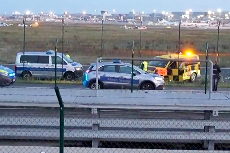 Mehrere Einsatzfahrzeuge der Polizei stehen unweit des Rollfelds am Frankfurter Flughafen - der Airport wurde durch eine Protestaktion der "Letzten Generation" am Donnerstagmorgen blockiert.