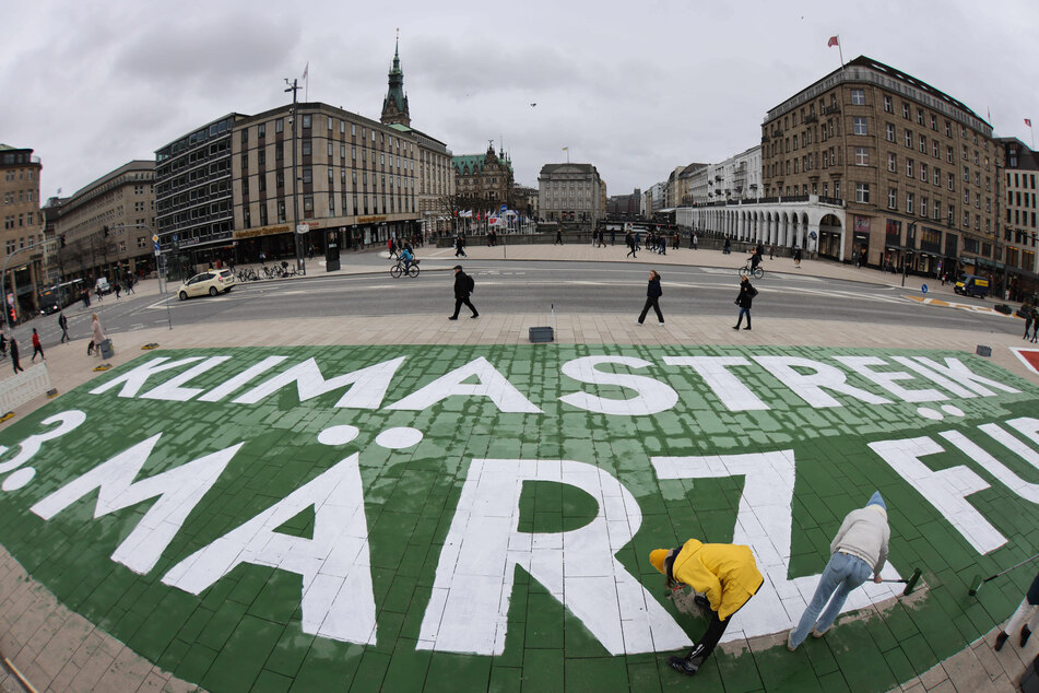 Aktivisten und Aktivistinnen der Klimabewegung Fridays for Future malen einen Protesttext auf den Jungfernstieg nahe dem Rathaus.