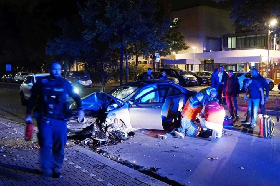 Rettungskräfte kümmern sich um den neben dem Auto liegenden Unfallfahrer.