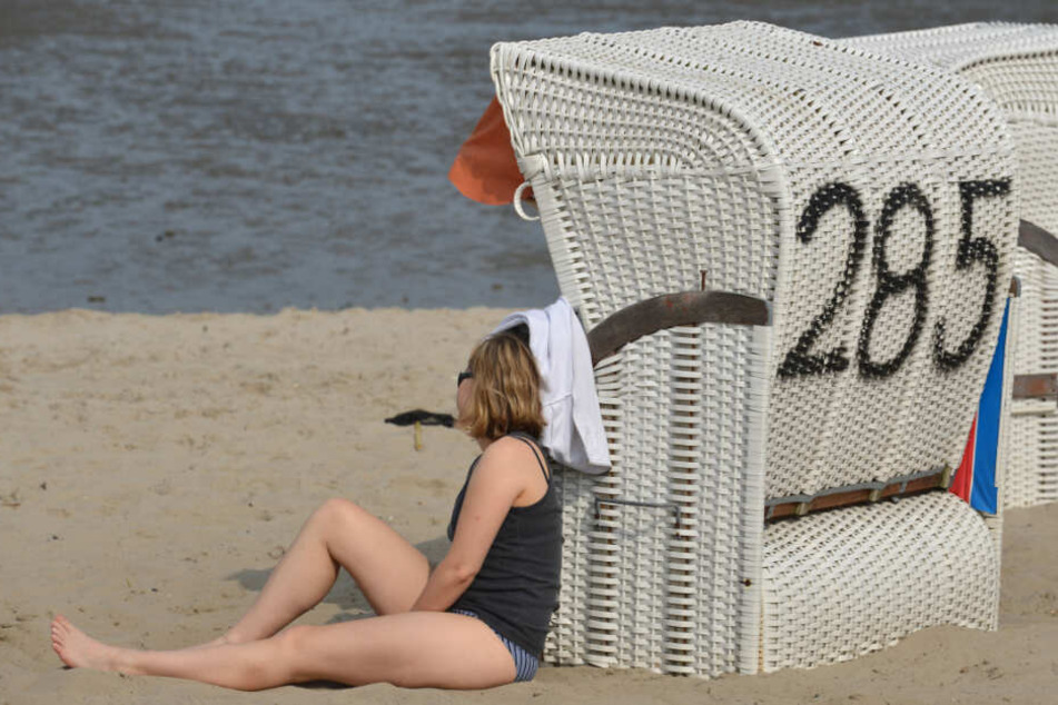 Eine junge Frau sonnt sich an einem Strandkorb an der Nordsee. (Archivbild)