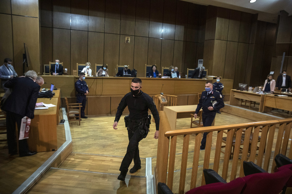 Polizeibeamte gehen mit Mund-Nasen-Schutz beim Prozess gegen die rechtsextreme griechische Partei (Golden Dawn) "Goldene Morgenröte" durch den Gerichtssaal.