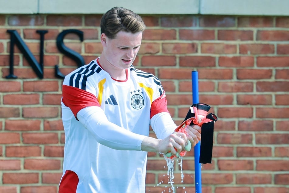 Trainingstorhüter Jonas Urbig wringt seine Handschuhe aus, die vorher in Eiswasser lagen.