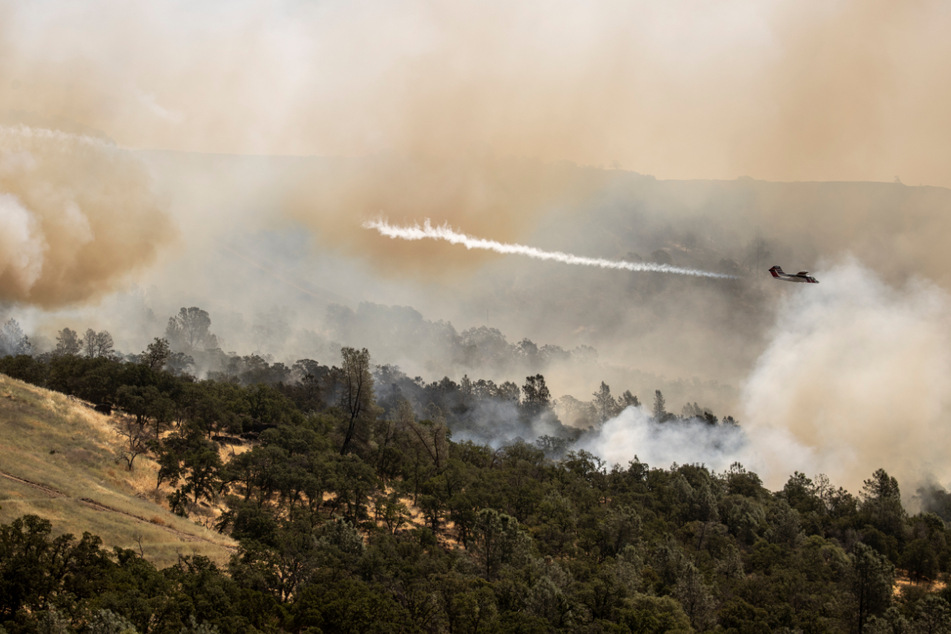 Ein Lufttransportflugzeug vom Typ Cal Fire OV-10 wirft Feuerlöschmittel über einem Waldbrand ab.