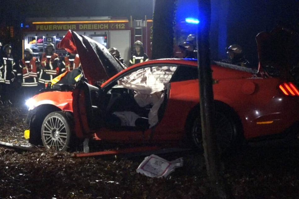 Einsatzkräfte der Feuerwehr stehen hinter dem zerstörten Sportwagen.