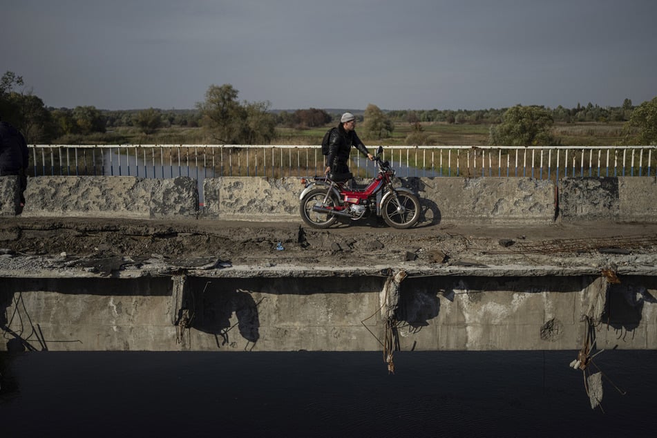 in Mann zieht sein Motorrad auf einer zerstörten Brücke über den Fluss Oskil während einer Evakuierung in Kupjansk.