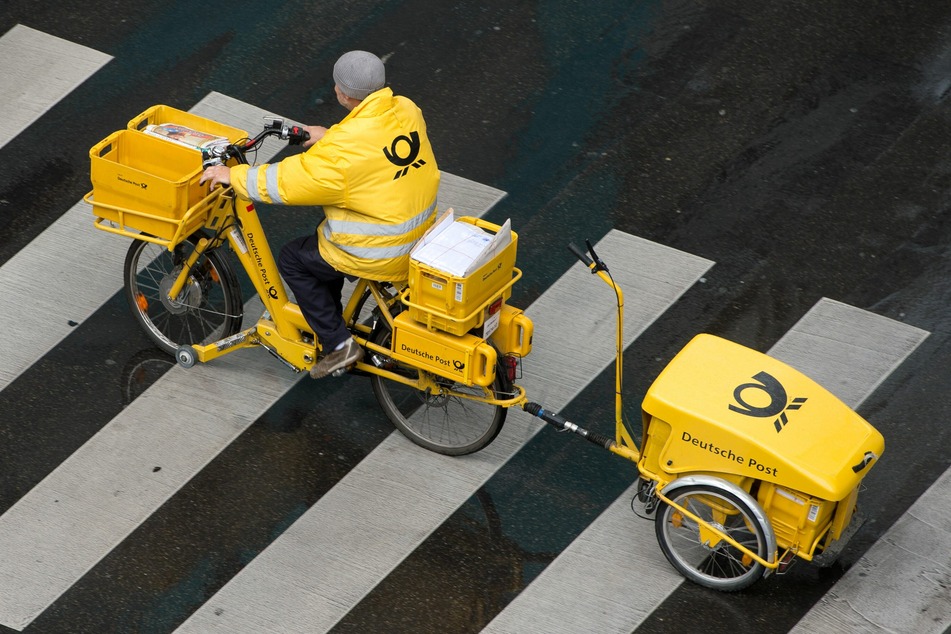 Ein Briefträger der Deutschen Post fährt mit einem Fahrrad (E-Bike) über einen Zebrastreifen.