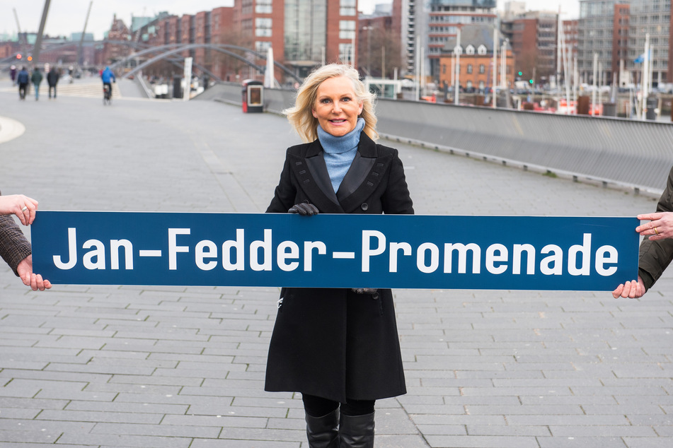 Marion Fedder, Witwe des Schauspielers Jan Fedder (†64), steht am Hafen und hält ein Schild mit der Aufschrift "Jan-Fedder-Promenade".