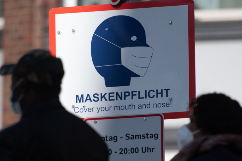 Passanten gehen in der Innenstadt an einem Schild mit der Aufschrift "Maskenpflicht" vorbei.