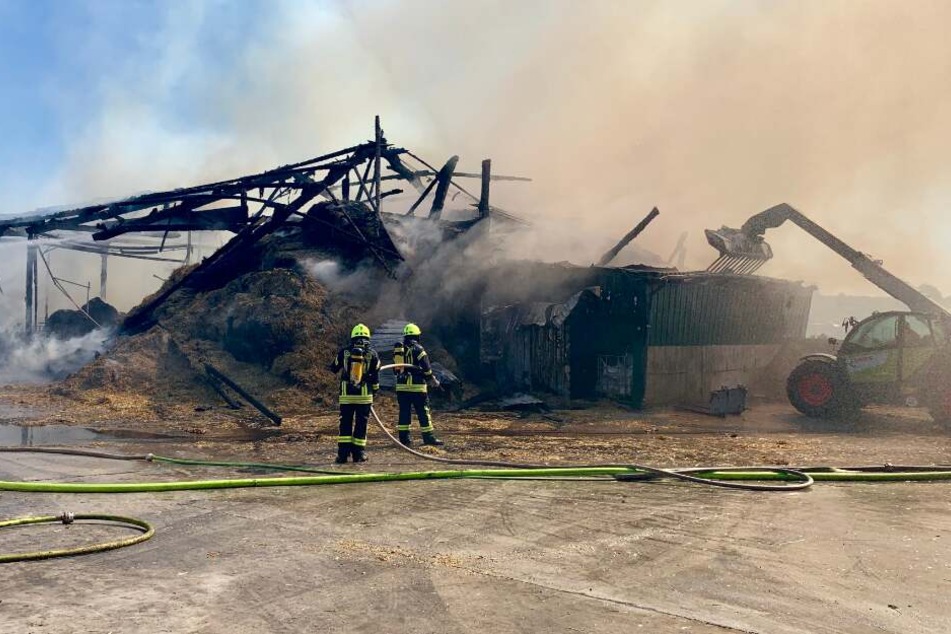 Feuerwehrleute stehen vor den rauchenden Trümmern.