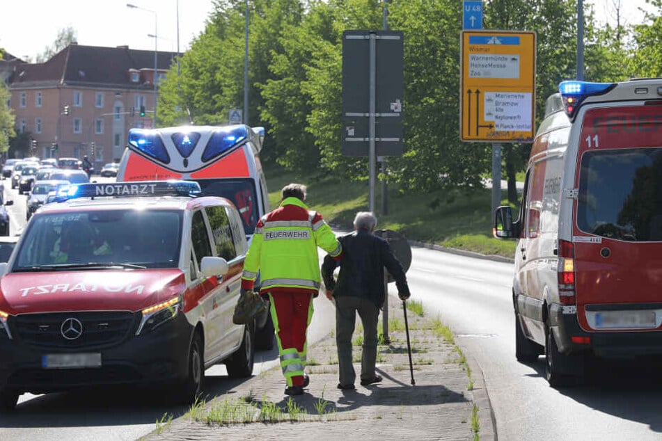 Ein Beamter der Feuerwehr muss den Unfallfahrer, einen 82-jährgen Senior, der am Stock geht, nach dem Unfall stützen.