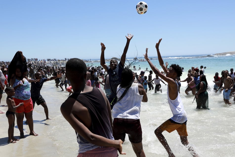 Menschen spielen Ball und genießen den Neujahrstag am Strand von Camps Bay.