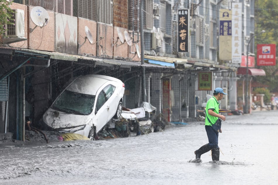 A man walks past a damaged car, swept away by floodwaters, in Hualien on September 24, 2025, following the bursting of a barrier lake during the passing of Super Typhoon Ragasa.