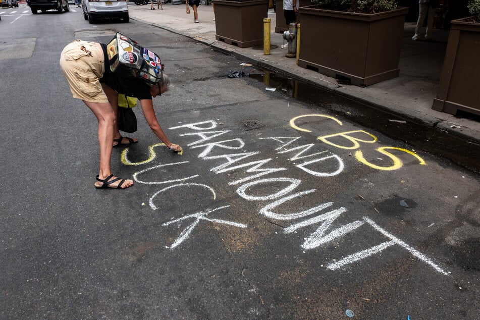 A woman writes "CBS and Paramount Suck" in chalk outside of the Ed Sullivan Theater in New York City.
