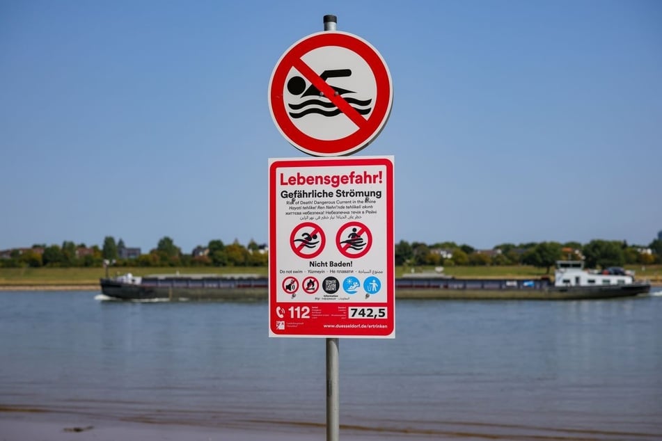 Schilder am Rheinufer wie hier in Düsseldorf weisen auf die Gefahren des Schwimmens im Rhein hin.