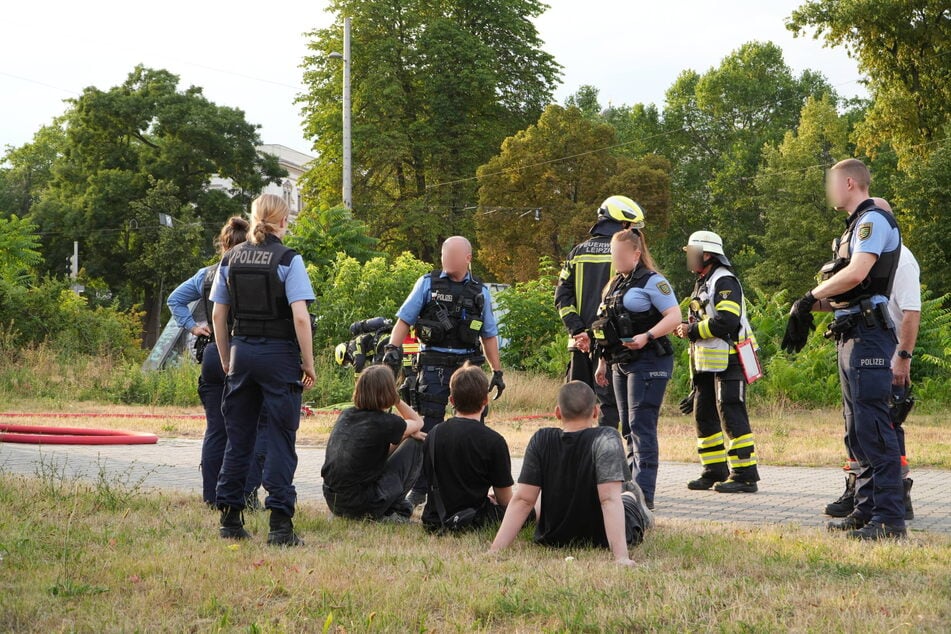 Unter Tatverdacht: Polizisten befragen die im Gras sitzenden Jugendlichen nach dem Brand im alten Bowlingtreff.