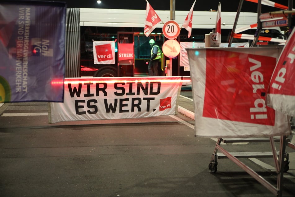Ein Banner mit der Aufschrift "Wir sind es wert" hängt an einer Schranke am Betriebshof der Kölner Verkehrs-Betriebe (KVB).