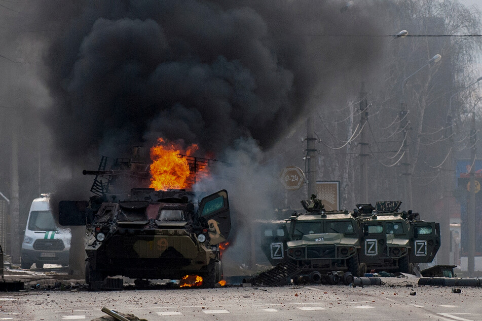 Ein gepanzerter Mannschaftswagen brennt und beschädigte Nutzfahrzeuge stehen nach Kämpfen in Charkiw auf einer Straße.