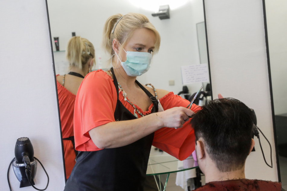 A hairdresser with a facial mask cuts a client's hair.