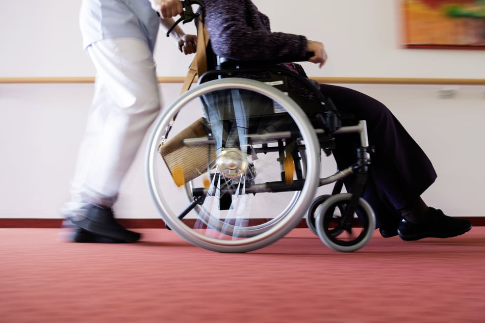 Ein Pfleger schiebt eine Bewohnerin eines Pflegeheims in einem Rollstuhl über den Flur. Zum internationalen Tag der Pflege am 12. Mai demonstrieren Pflegende mit vielfältigen Aktionen für bessere Arbeitsbedingungen. (Symbolbild)