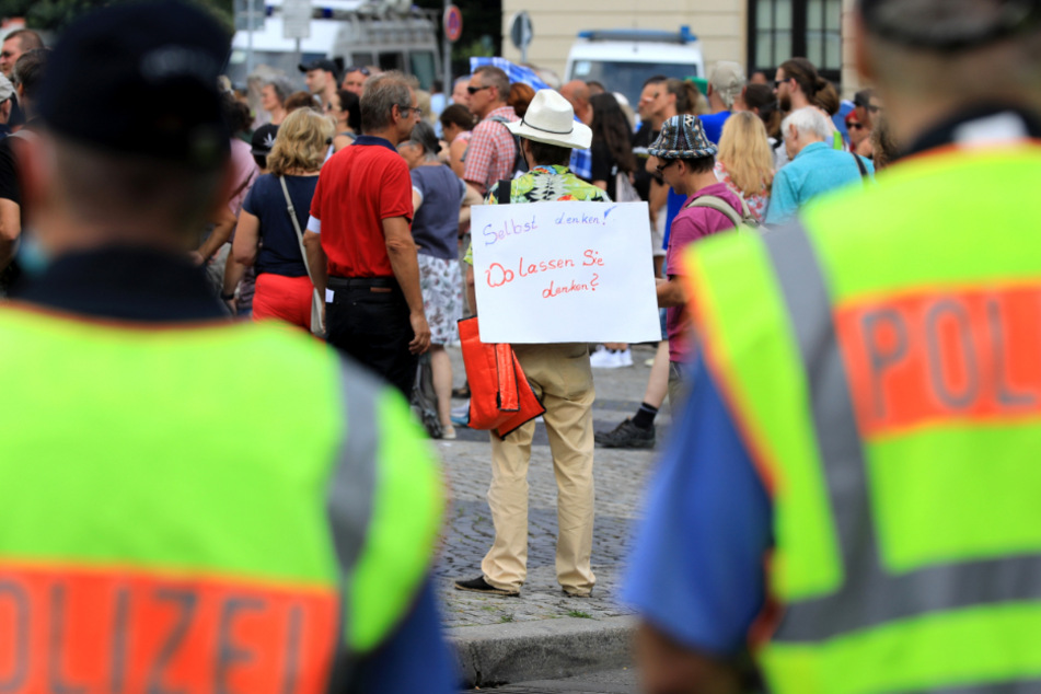 Magdeburg: Polizisten beobachten die Kundgebung des Organisationsteams "Team Querdenken - 391" unter dem Motto "Recht auf Leben" auf dem Alten Markt. Vor ihnen steht ein Teilnehmer der Kundgebung mit einem Schild mit der Aufschrift "Selbst denken! Wo lassen Sie denken?".